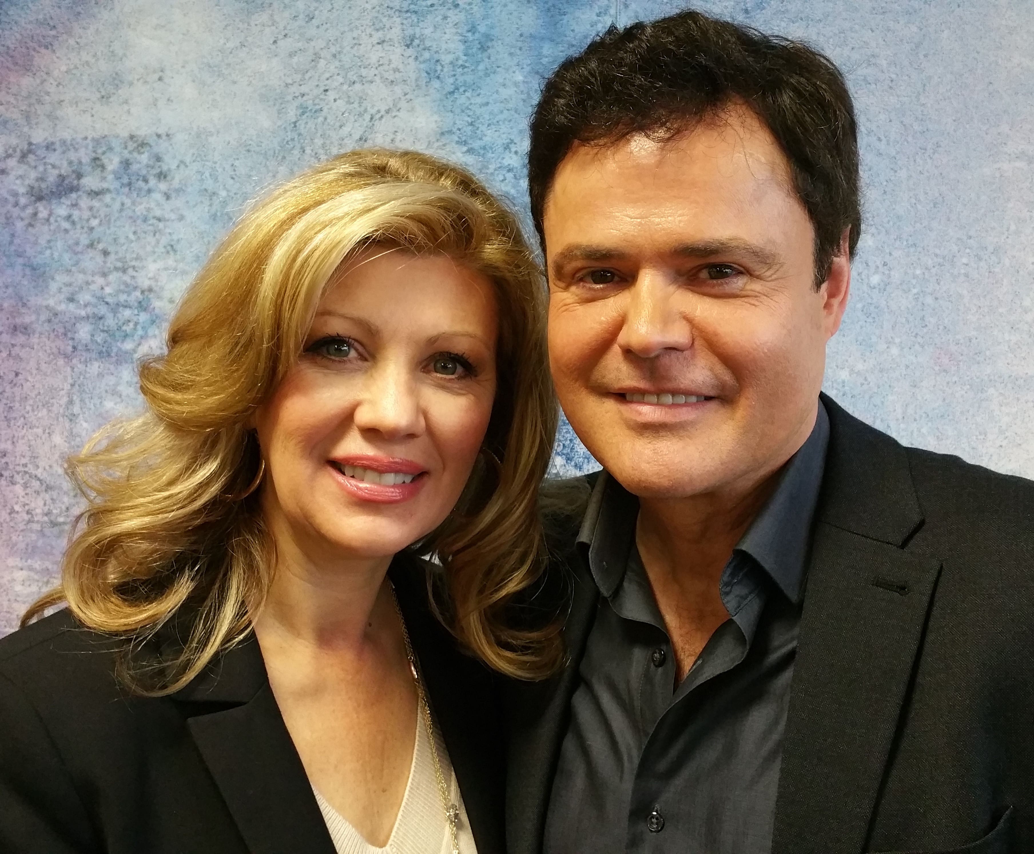 Donny Osmond in a black formal suit with his wife in a white vest and black coat.